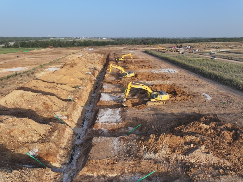 Excavators digging a long utility trench across an open site