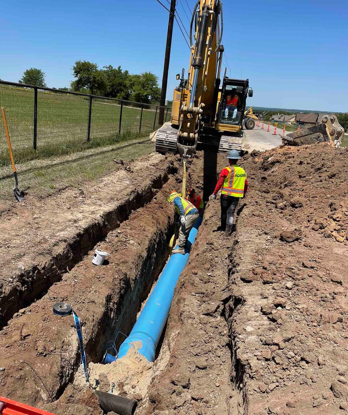 Excavator and crew lowering water line pipe into a trench