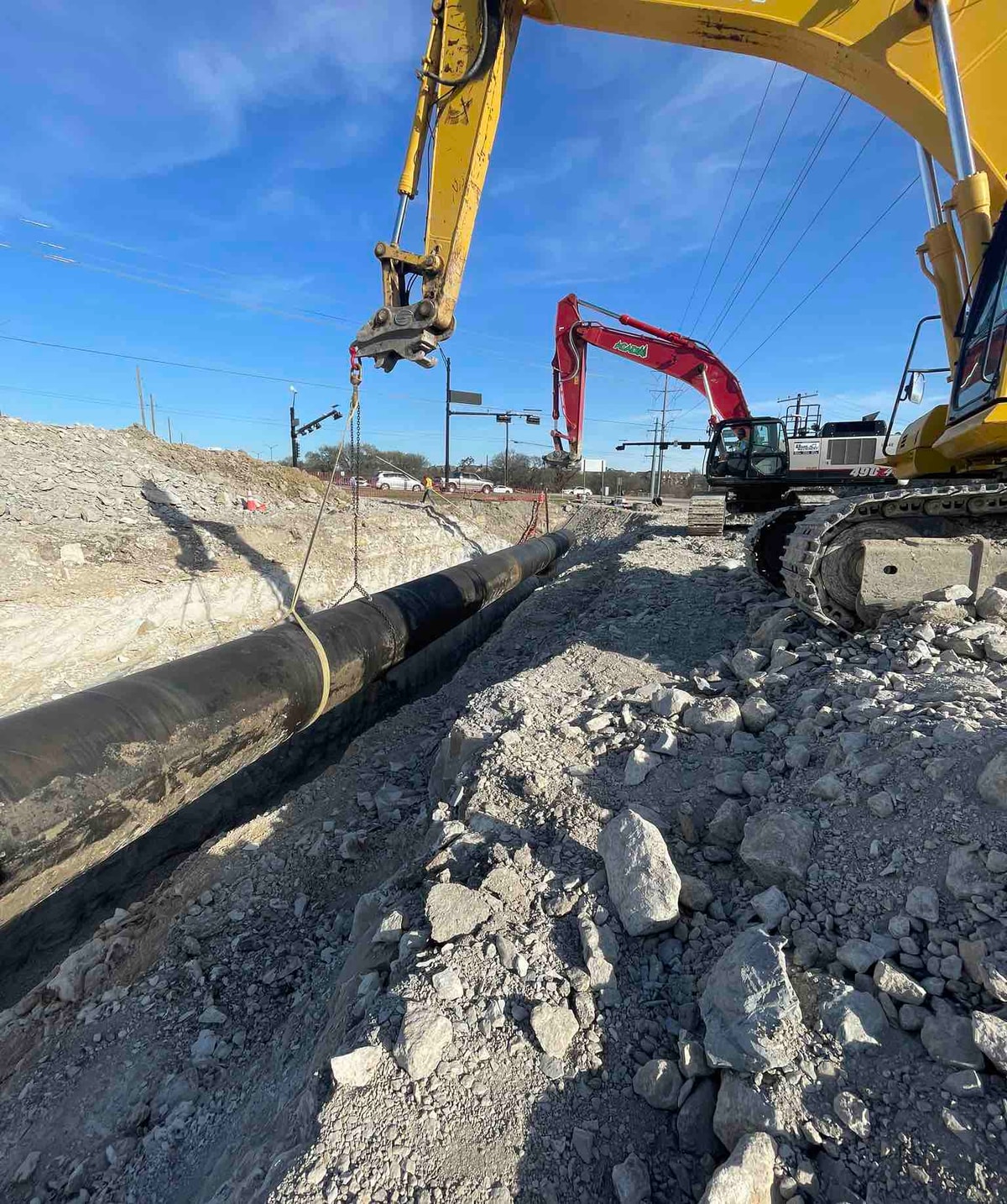 Excavator lowering pipe into a water line trench